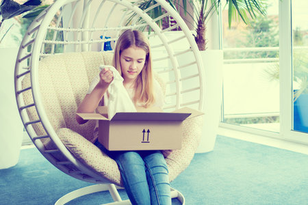 blond girl sitting in chair and opening a packageの写真素材