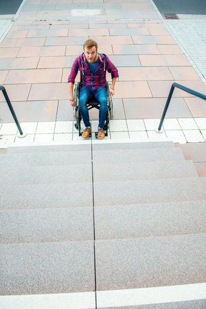 young disabled man in wheelchair in front of stairs from aboveの写真素材