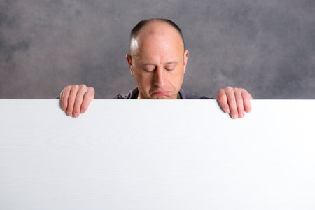 young man with a white advertising board in front of gray backgroundの写真素材