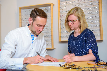 in optician shop- young woman and man selecting new glassesの写真素材