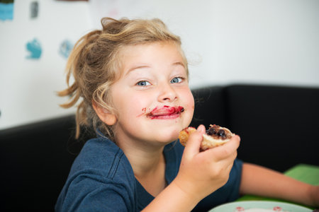 funny girl eating bread roll with dark marmeladeの写真素材