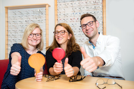in optician shop-two women and one man with thumb up selecting new glassesの写真素材
