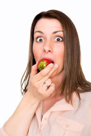 Nice young woman eating strawberry looking surprisedの写真素材