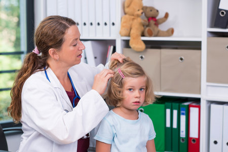 female pediatrician in white lab coat examined little girl for liceの写真素材