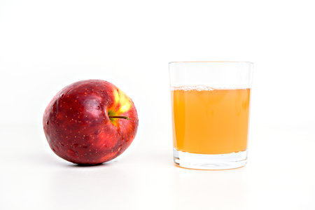 red apple with glass of naturally cloudy juice in front of white backgroundの写真素材