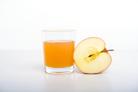 half apple with glass of naturally cloudy juice in front of white backgroundの写真素材