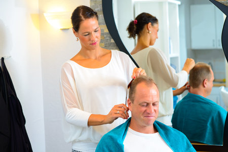 female hairdresser cutting hair of man in her shopの写真素材