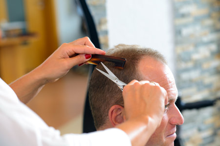 female hairdresser cutting hair of man in her shopの写真素材