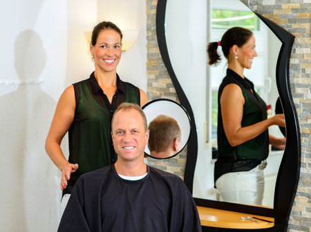 female hairdresser cutting hair of man in her shopの写真素材