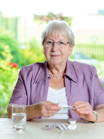 female senior with drugs sitting at tableの写真素材
