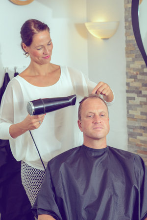 female hairdresser cutting hair of man in her shopの写真素材