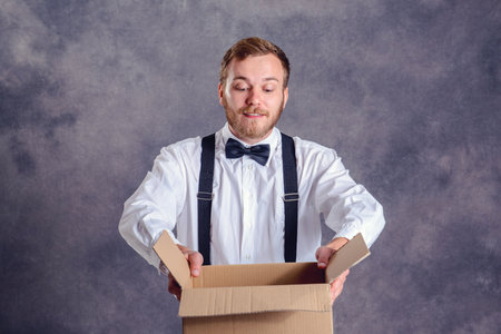 Young man opening a package in front of gray backgroundの写真素材
