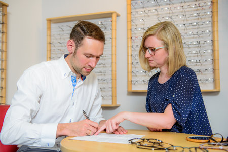 in optician shop- young woman and man selecting new glassesの写真素材