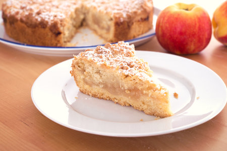 A piece of apple pie with crumbles in a white plate on wooden tableの写真素材
