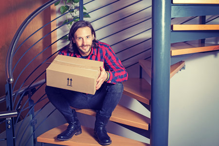 young man sitting in corridor and opening a packageの写真素材
