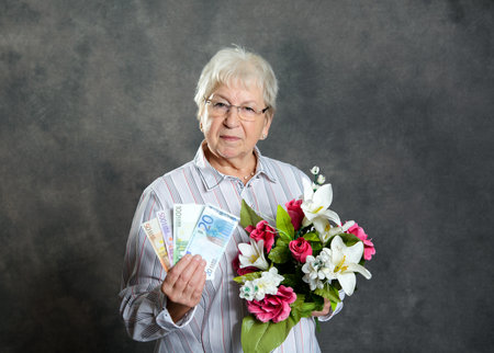 gray hairy elderly woman with flowers and moneyの写真素材