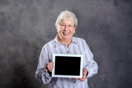 gray hairy elderly woman showing tablet pc and smilingの写真素材
