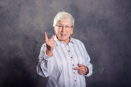 Gray hairy elderly woman looking angry and showing forefingerの写真素材
