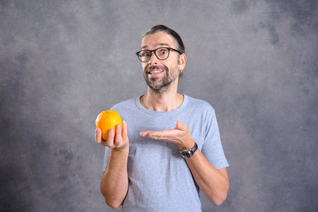 long haired young man with orange in front of gray background