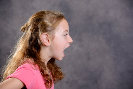 angry girl with blond hair and pink shirt in front of gray backgroundの写真素材
