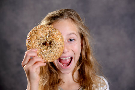nice blond girl in front of gray background looking through a big bagelの写真素材