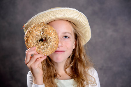 nice blond girl with straw hat in front of gray background looking through a big bagelの写真素材