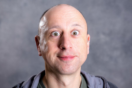 young baldheaded man in front of gray background looking amazed in to the cameraの写真素材