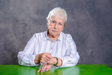 gray hairy elderly woman sitting at table and set her watchの写真素材