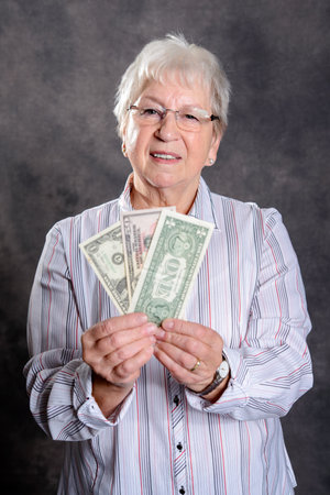 happy gray hairy elderly woman with money in front of gray backgroundの写真素材