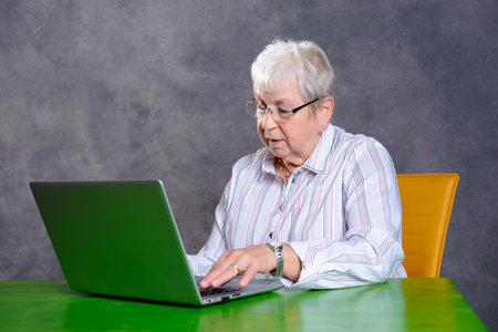 gray hairy elderly woman using laptop on table