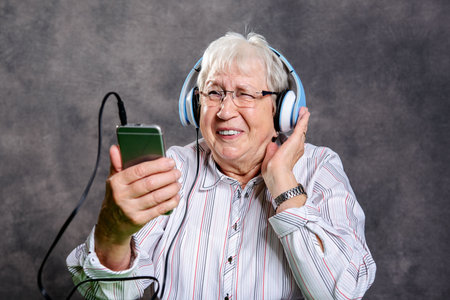 gray hairy elderly woman listening music with headphoneの写真素材