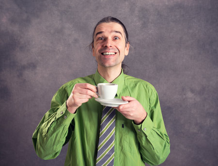 young man in green shirt and necktie drinking coffee in front of gray backgroundの写真素材