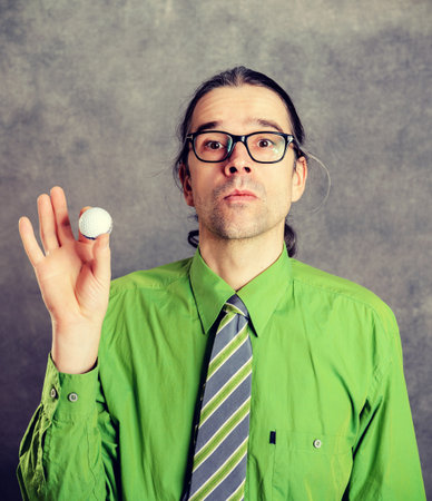 young business man in green shirt and necktie with golf ball in front of gray backgroundの写真素材