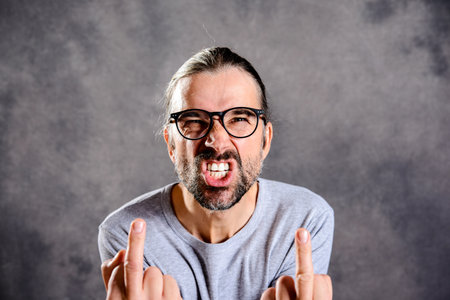 young man in front of gray background showing middle fingerの写真素材