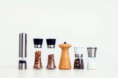 different spice mills with salt,pepper and other herbs in front of white backgroundの写真素材