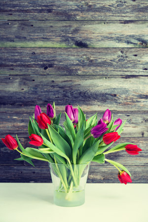 bouquet of red and violet tulips  in vase in front of wooden backgroundの写真素材