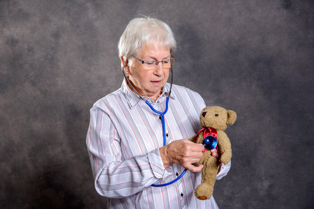 gray haired grandmother with stethoscope is puppet doctor for teddy bearの写真素材