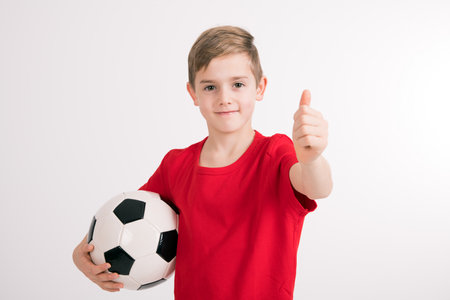 boy in red shirt with soccer ball and thumb up in front of white backgroundの写真素材