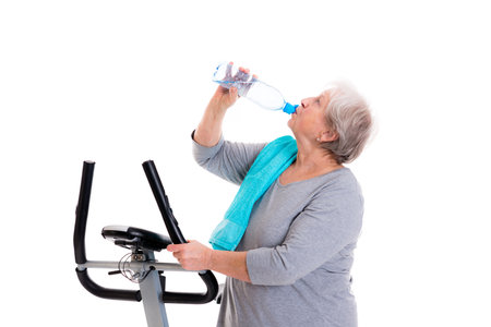 gray-haired female senior with water bottle train with fitness machineの写真素材