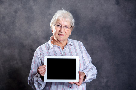 gray hairy elderly woman showing tablet pc and looking amazedの写真素材