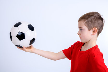 boy in red shirt with soccer ball in front of white backgroundの写真素材