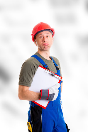 young workman in blue dungarees with clipboard looking scepticalの写真素材