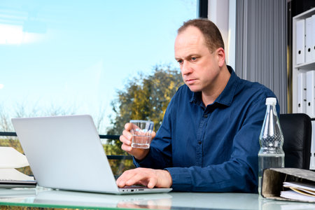 A young business man at his desk drinking waterの写真素材