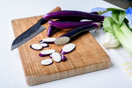 japanese eggplant on wooden board with cooking knife and pak choi saladの写真素材