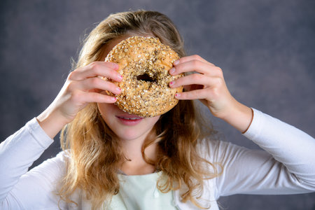 nice blond girl in front of gray background looking through a big bagelの写真素材