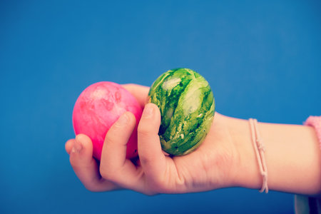 child hand with green and pink easter egg on blue groundの写真素材