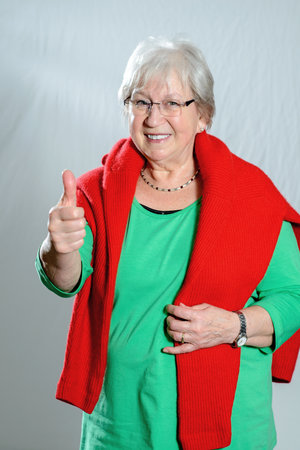 gray haired female senior with thumb up in front of gray backgroundの写真素材
