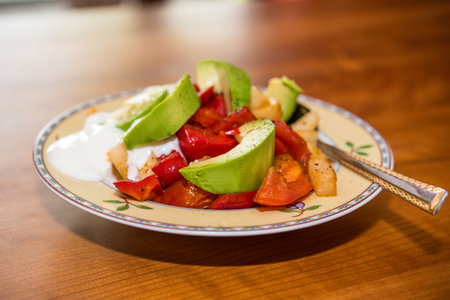 plate with fried vegetables and row avocado on wooden groundの写真素材
