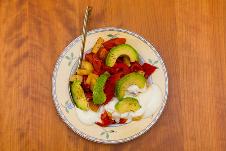 plate with fried vegetables and row avocado on wooden groundの写真素材