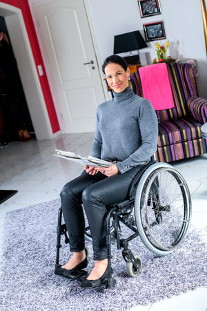 young disabled woman in wheelchair at home reading newspaper and drinking coffeeの写真素材